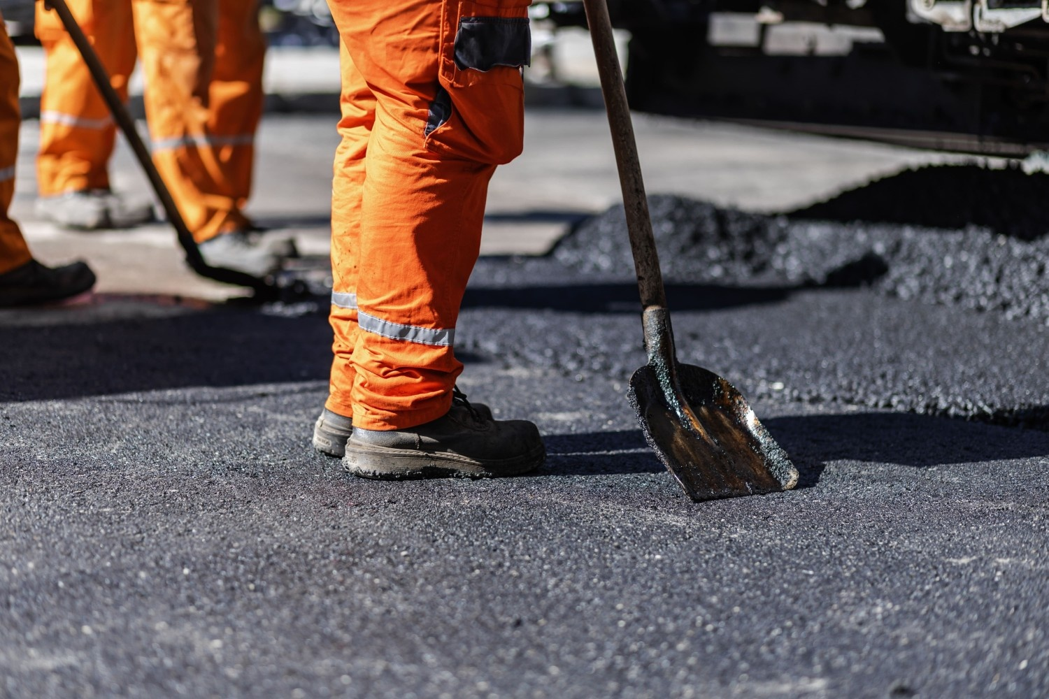Asphalt-paving-services Construction workers using heavy equipment to lay fresh asphalt on a roadway during an asphalt paving project